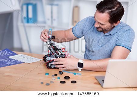 Work is fun. Smiling man in his forties in the process of making a little robot