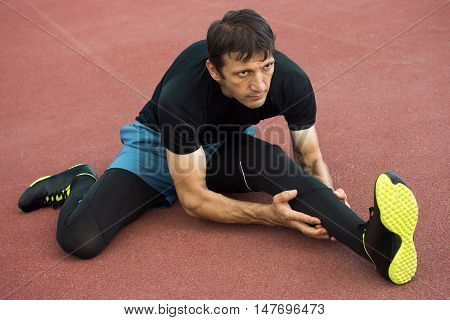 The athlete sportsman is stretching his legs outdoors.