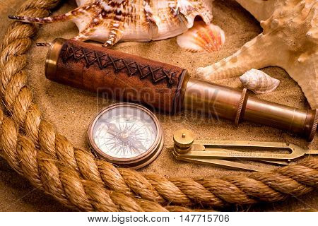 Compass with spyglass and rope on sand background