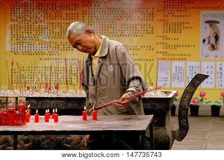 Chengdu China - September 20 2006: An elderly Chinese man lighting incense sticks from burning red candles at the Da Ci Buddhist Temple