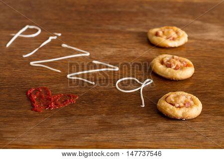 Three mini pizzas with sausage and cheese on wood table. Painted heart of ketchup and written text 
