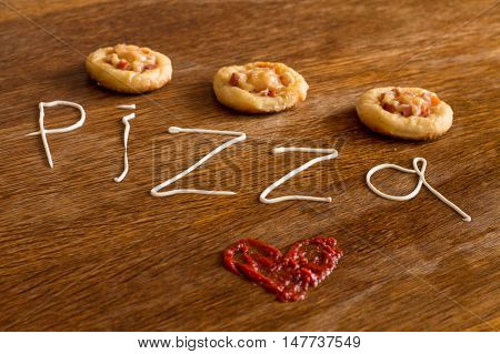 Three mini pizzas with sausage and cheese on wood table. Painted heart of ketchup and written text 