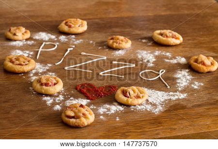Heart of mini pizzas with sausage and cheese on wood table.  Painted heart of ketchup, written text 