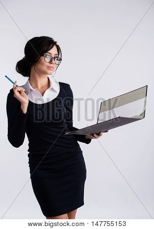 Young Caucasian woman wearing a dark blue dresst and and a white shirt, holding a ring binder folder and pen. Isolated on light background