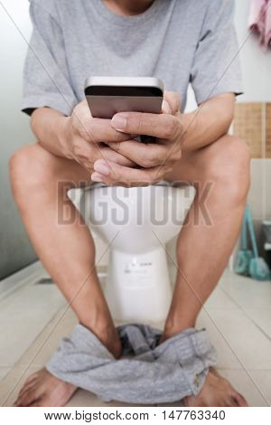A guy using mobile phone while sitting in toilet, selective focus