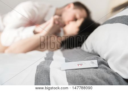 Positive pregnancy test is laying on the bed. Happy couple enjoyed on background