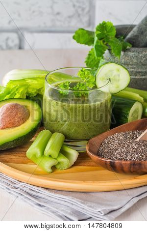 Healthy green juice smoothie surrounded by avocado, cucumber,  celery and chia seeds on white background
