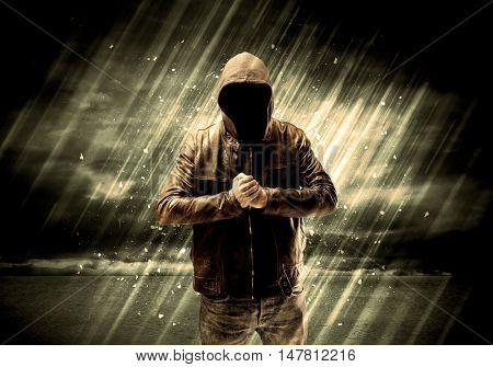 An incognito hooded stalker standing in the rain with his back in front of dark scary landscape concept