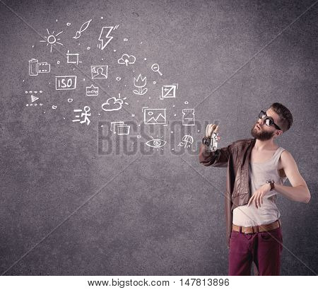 An elegant hipster guy trying to use a vintage camera with camera settings icons drawn on wall, like flash, white balace or ISO value concept