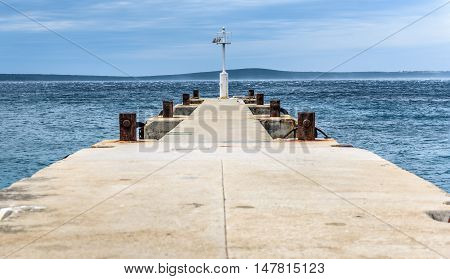 Old pier with a lighthouse beacon and calm sea. Rusty moorings and seagulls on concrete pier on a windy day with dramatic clouds. Adriatic sea - Silba Croatia.