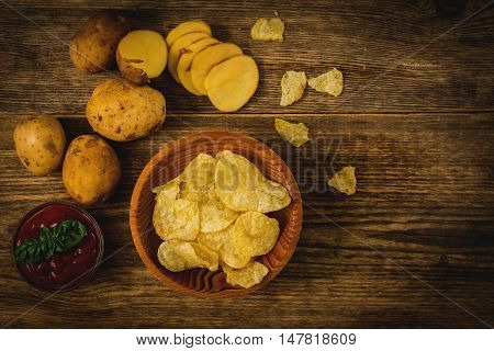 Salty potato chips snack with tomato dip on wood table top view