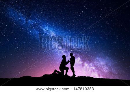 Milky Way. Night landscape with silhouettes of a man making marriage proposal to his girlfriend and starry sky. Silhouette of lovers. Couple relationship. Milky way with people. Universe