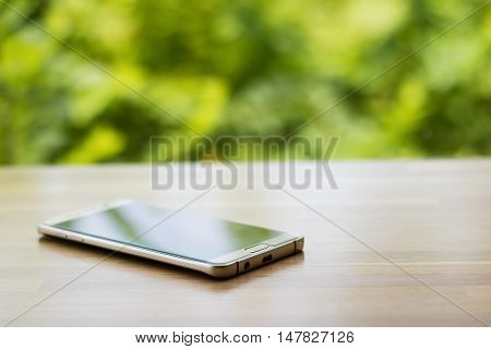 Gold smartphone on wooden table with blurry green tree background selective focus. Put down your smart phone concept