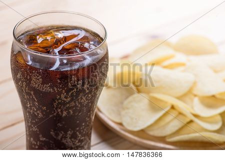 Potato chips in bowl and cola on wooden background