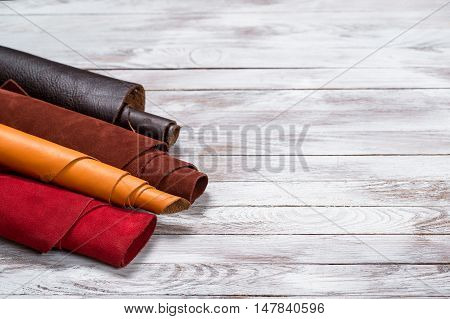 Brightly colored leather in rolls on the white wooden background. Leather craft. Copy space.