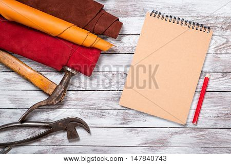 Brightly colored leather in rolls working tools shoe lasts notebook with pencil on white wooden background. Leather craft.