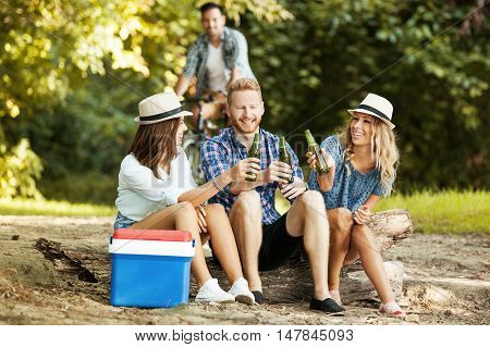 Group of friends is sitting on stump while their friend is coming by bike.