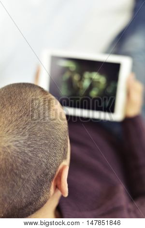 a young caucasian man lying on the couch watches a movie or a series in streaming in his tablet computer