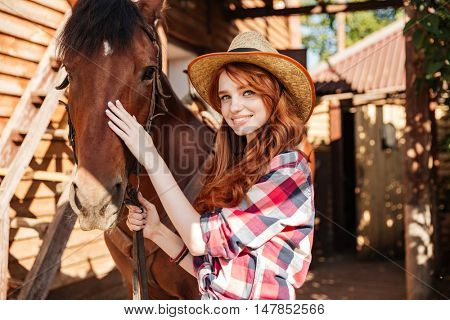 Happy redhead young woman cowgirl with her horse in village
