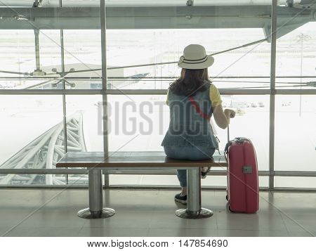 Single woman with pink suitcase sit and see outside at the airport