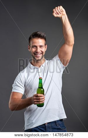 A handsome young man feeling happy and celebrating while holding a beer