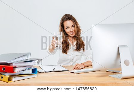 Young brunette businesswoman sitting at the table with computer holding glass of water isoltaed on the white background