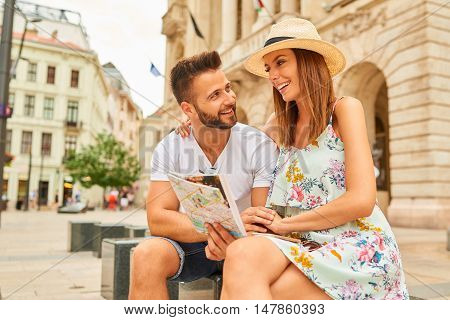 A beautiful young couple are sitting and holding a map and looking around at the Egyetem Square in Budapest, Hungary.