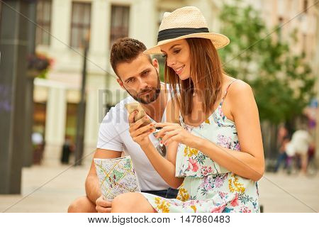 A beautiful young couple are sitting and using a smartphone at the Egyetem Square in Budapest, Hungary.
