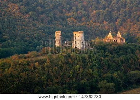 Sunlit ruins of Chervonohorod Castle against autumn trees background.