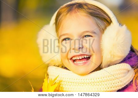 Happy little girl in earflaps in the autumn park