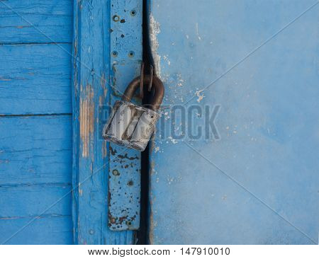 Gray metal lock hangs on a blue painted door closeup