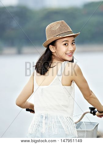 young and beautiful asian girl turning to camera smiling while riding bicycle
