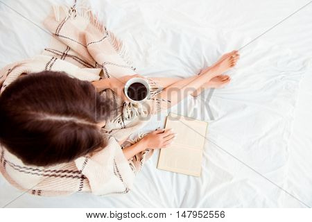 Top View Of Young Woman Reading Book And Basking With Plaid And Coffee
