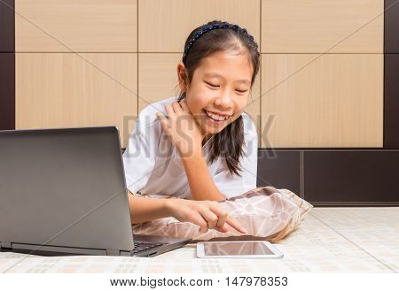 Happy Asian female teenager using technology interacting with moblie computer tablet device in her bed