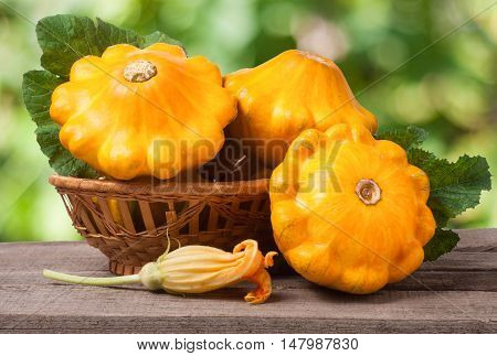 yellow pattypan squash with leaf in a wicker basket on a wooden table with a blurred background.