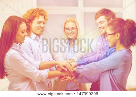 business, office, gesture and startup concept - smiling creative team with hands on top of each other sitting in office