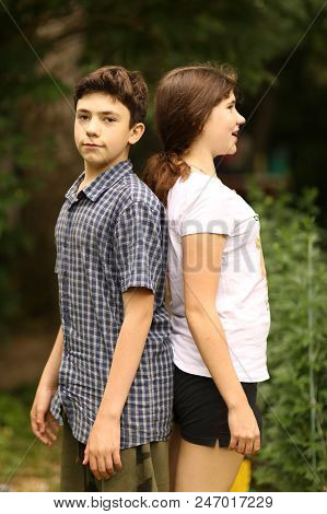 Two Siblings Teenager Kids Sister And Brother Measure Height Each Other On Green Garden Background
