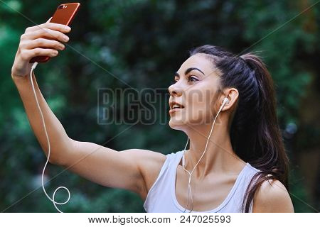 Young Girl Is Taking Picture Of Herself Using Red Cell Phone And Listening To The Music Using White 