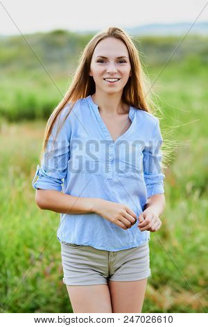Happy Smiling Young Girl In Blue Shirt And Shorts In The Field