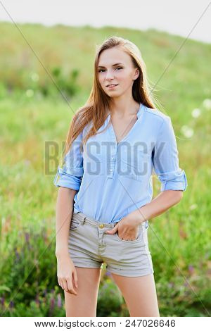Happy Smiling Young Girl In Blue Shirt And Shorts In The Field
