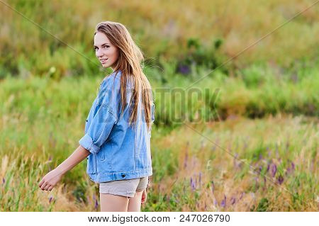 Happy Smiling Young Girl Wearing Blue Jeans Jacket And Shorts Is Standing In The Field