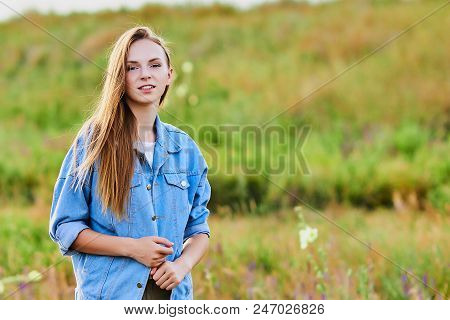Happy Smiling Young Girl Wearing Blue Jeans Jacket And Shorts Is Standing In The Field