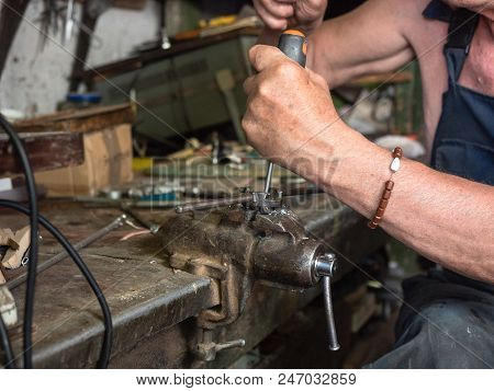 Older Man Sitting At Workbench And Working. Human's Hands In Process Of Screw Cutting, Close Up View