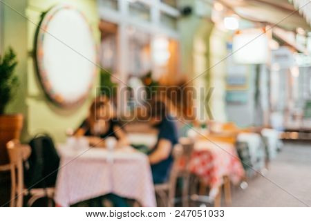 Blurred Background With Group Of Peolple Sitting At The Cafe Veranda Outside.