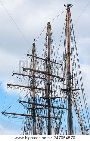 Masts And Rigging Of A Historic Three-master Sailing Ship Against The Cloudy Sky, Travel And Voyage 