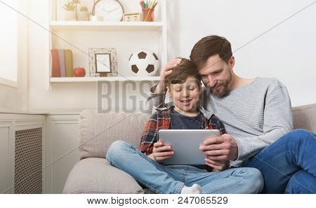 Father And Son Spending Time Together And Playing On Digital Tablet On Sofa At Home