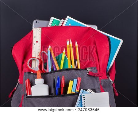 Closeup Of A Bookbag With An Assortment Of School Supplies On A Blackboard Background