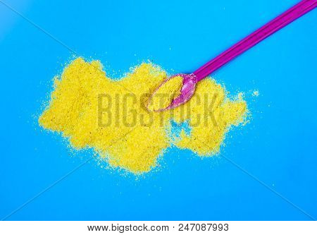 Yellow Powder On A Blue Background And Plastic Spoon. Spice Or Juice Powder Or Something Similar