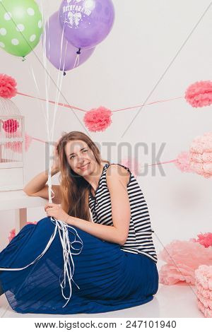 The Blonde Smiles And Looks At The Camera Between The Colored Balls On A White Background. Studio Po