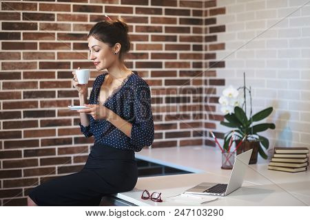 Smiling Business Woman, Enjoing A Cup Of Coffee While Sitting On The Table In The Office, Wearing Bl